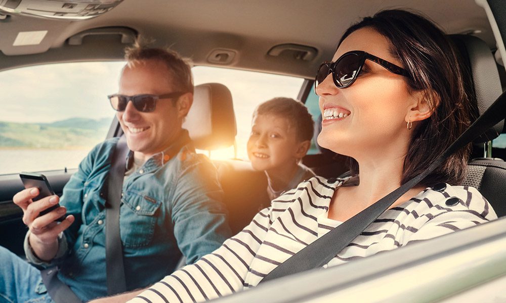 Blog - Family and Smiling in the Family Car While the Mom is Driving and the Dad is on the Phone